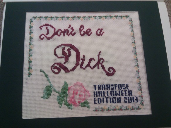 Cross-stitch with the main slogan "Don't be a Dick", a smaller type showing "Transpose Halloween Edition 2013" and some chintzy flowers